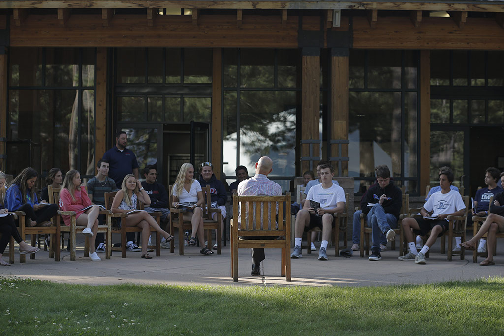 precollege-faq-2 a group of students at a Launch event sitting in chairs outside with an instructor in front of them all speaking to them