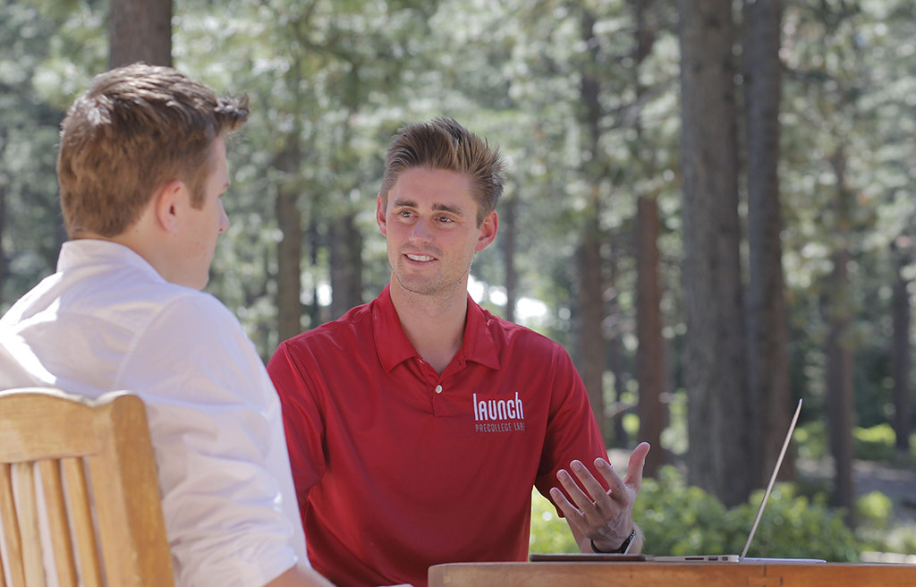 precollege-faq-4 an image of a Launch teacher speaking one-on-one with a student while sitting in chairs outdoors